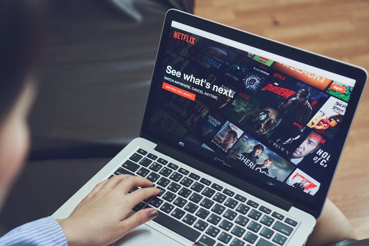 Une jeune femme devant son ordinateur regarde le menu de Netflix pour choisir un film